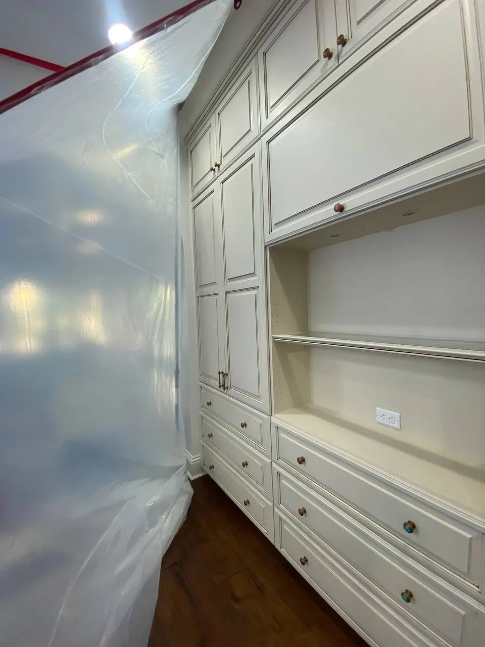 White kitchen cabinets being painted, covered with plastic sheeting