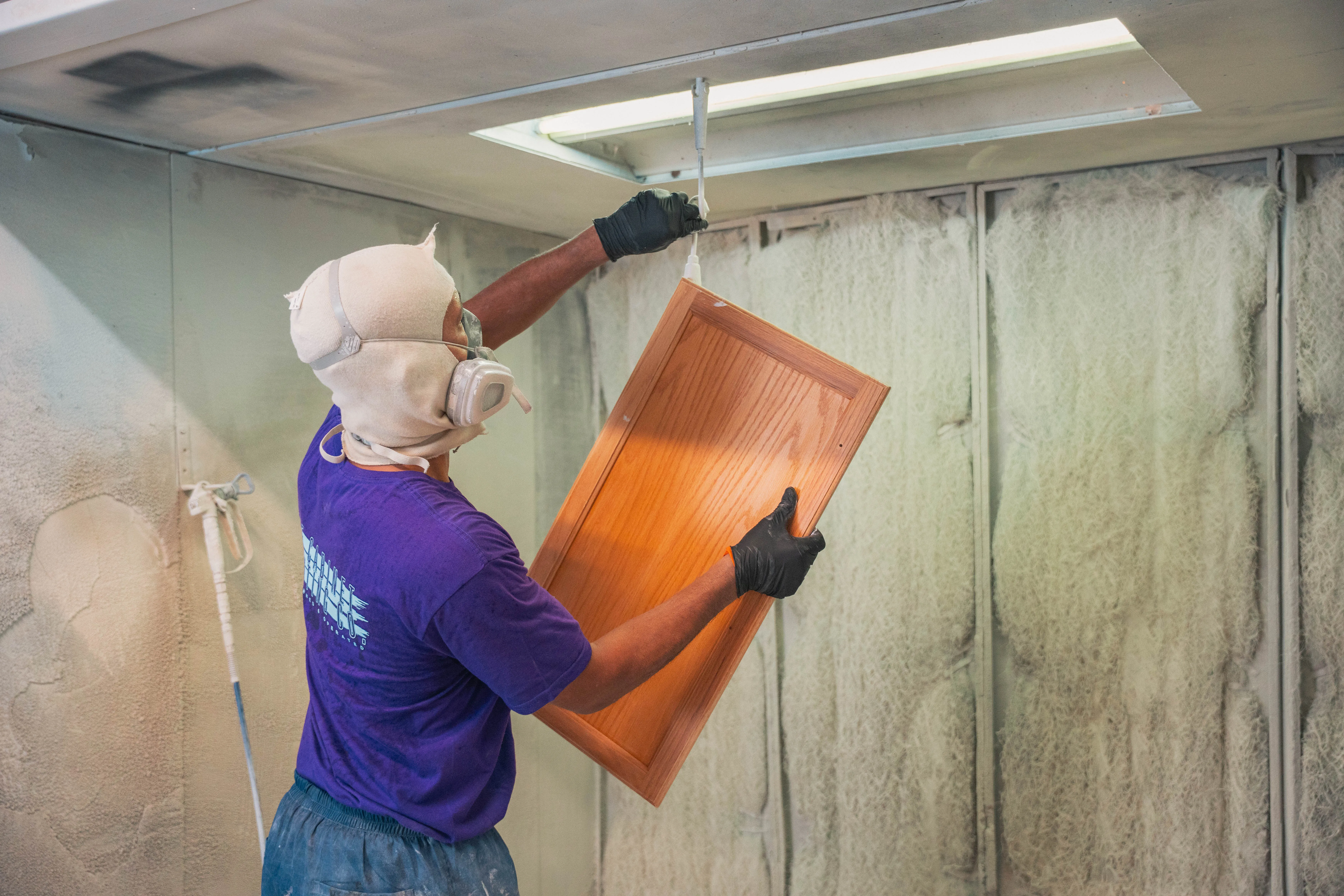 Cabinet door hanging in a spray booth before refinishing