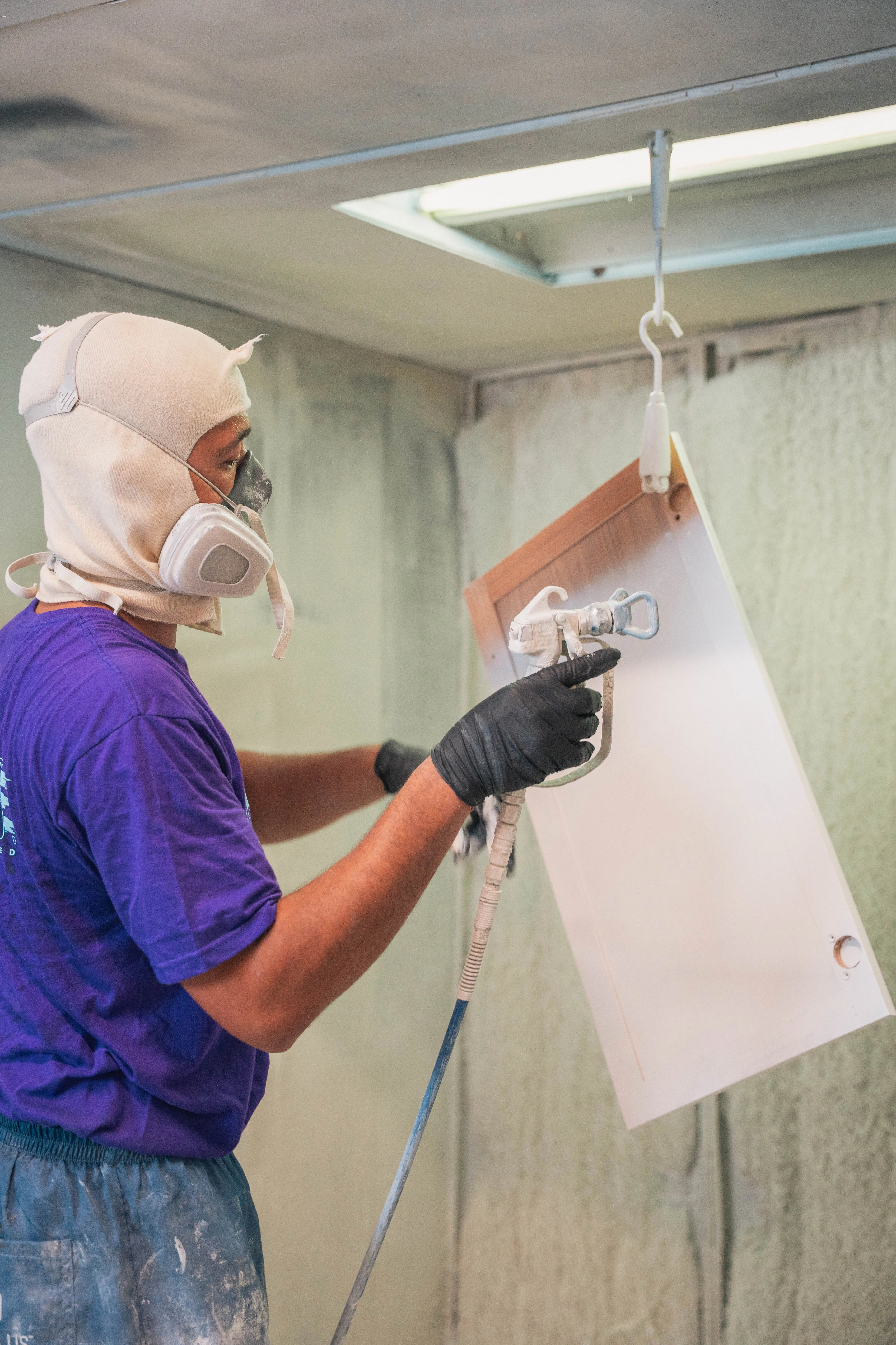 Cabinet door being spray painted with a white finish in a spray booth